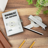 The tape dispenser beside its retail box on a desk with pencils and a notebook