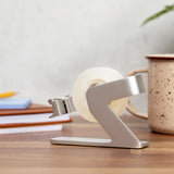 Side view of the silver tape dispenser showing its angled arm and weighted base on a desk