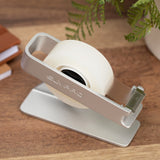 Close view of the silver dispenser and its serrated cutting edge, with a fern and books behind