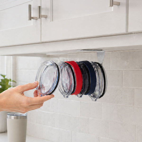 A hand taking a clear tumbler lid from a row of clear, red and navy lids hanging from the ELYPRO organizer under a white kitchen cabinet