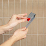 Hands peeling the red backing from the adhesive strip on the back of the bracket