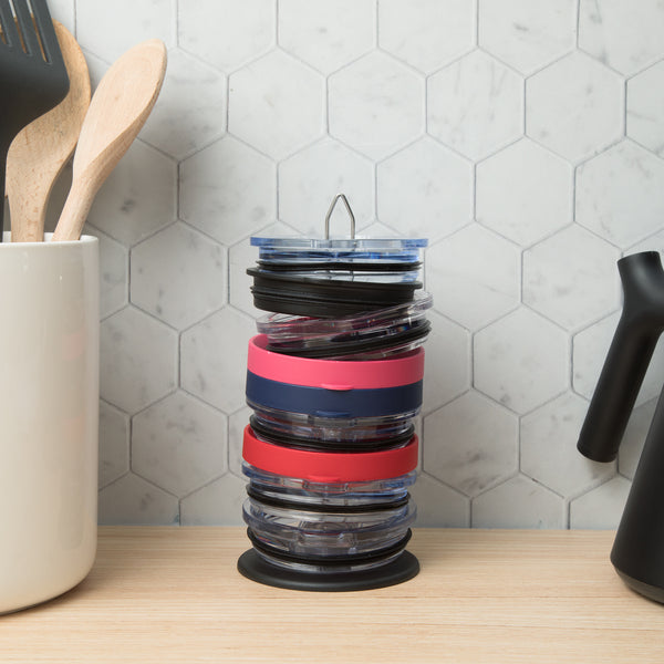 The organizer holding a stack of coloured tumbler lids on a wooden counter beside a utensil crock