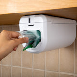Close-up of a hand taking a single bag from the dispenser in one motion
