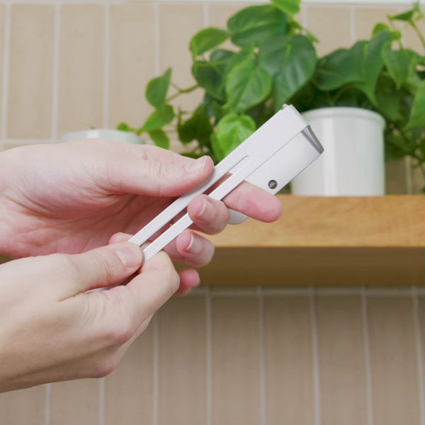 Hands holding the white ELYPRO Under-Cabinet Tumbler Lid Organizer rail before mounting it in a kitchen